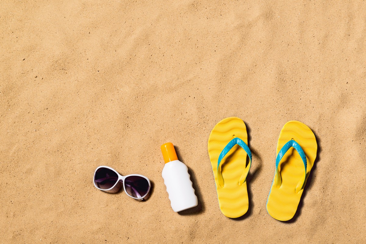 summer-vacation-composition-with-pair-of-yellow-flip-flop-sandals-sunglasses-and-sun-cream-on-a-beach-sand-background